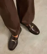 Zapato mocasín femenino de PU color negro, con punta cuadrada y detalle metálico dorado en el empeine. Tiene un tacón bajo y suela de goma.