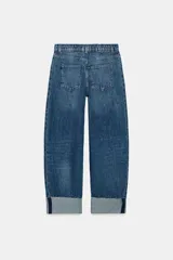 Jeans baggy de tiro medio con pernera holgada, diseño de cinco bolsillos y bajo acabado en vuelta. Cuenta con cintura elástica en la espalda y cierre frontal con cremallera y botón.