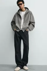 Sudadera tipo hoodie de corte relajado, confeccionada en tejido de algodón con textura estructurada y efecto lavado. Presenta cierre frontal con cremallera, cuello con capucha, manga larga, bolsillos tipo canguro y acabados en rib.