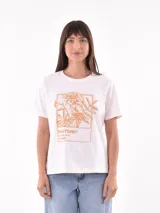Remera blanca de manga corta con estampado frontal de flores en tono naranja y un recuadro con la referencia de color Pantone "Marigold".