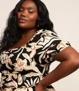 Blusa de crepé con estampado floral en tonos beige y negro, escote recto y mangas cortas abullonadas con puños elásticos.