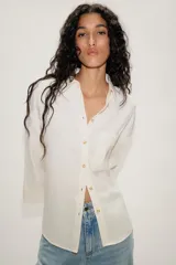 Camisa de corte oversize color marrón, con cuello solapa, mangas anchas por debajo del codo y bolsillo delantero de plastrón. Cierre frontal con botones.