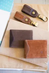 Set de billetera y llavero de cuero color marrón. La billetera es de cuero liso con costuras a tono y el llavero es de cuero texturizado con botón a presión y mosquetón metálico.