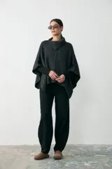 Capita de tejido de punto grueso en color gris oscuro, con cuello alto y diseño holgado tipo poncho.