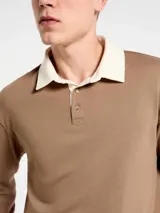 Buzo de estilo polo con cuello camisero en color crema y cuerpo en tono marrón. Presenta cierre frontal con botones, mangas largas y puños acanalados.