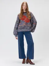 Sweater de punto con diseño geométrico y gráfico frontal en color rojo. Presenta cuello redondo, mangas largas holgadas y un ajuste suelto.