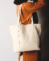 Bolso tipo tote de cuero natural color beige, con diseño minimalista, doble asa de hombro y cierre con broche. Incluye bolsillo interior y porta llaves.