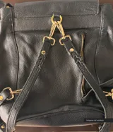 Cartera negra de cuero convertible en mochila, con tapa superior, cierre metálico, terminaciones trenzadas, forro de gabardina de algodón, bolsillos internos y externos con cierre.