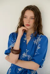 Vestido midi azul con estampado floral blanco, cuello en V, mangas cortas abullonadas y cierre frontal de botones. Incluye un lazo ajustable para la cintura.