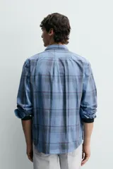 Camisa de corte regular fit confeccionada en tejido ligero de algodón, con estampado de cuadros en tonos azules y grises. Presenta cuello abotonado, manga larga con puños abotonados, bolsillo plastrón en el pecho y cierre frontal de botones.