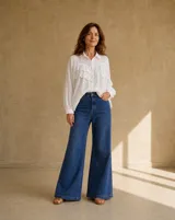 Camisa blanca de manga larga con cuello camisero, cierre frontal de botones y detalles de volados con bordado broderie en el frente.