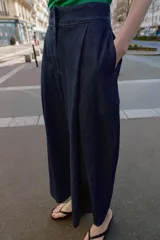 Pantalón tipo culotte de tiro alto confeccionado en denim azul oscuro. Presenta pinzas delanteras, pernera ancha y corta, bolsillos laterales ocultos y cierre frontal con cremallera, botón y ganchos.