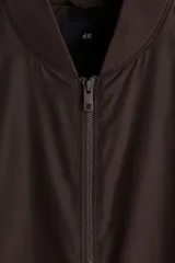 Campera bomber de color marrón oscuro, con cuello, puños y bajo acanalados. Posee cierre frontal y bolsillos laterales con cierre.