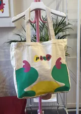 Bolso tipo tote de lona color crudo con asas de tela. Estampado con el logo 'picú' y diseño abstracto en colores amarillo, verde y fucsia.
