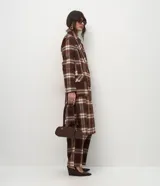 Trench coat largo de corte clásico con estampado de cuadros en tonos marrones y beige. Presenta cuello con solapas, cierre frontal con botones, mangas largas y bolsillos laterales aplicados.
