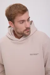 Hoodie color beige de manga larga con capucha, corte relajado, interior afelpado, bolsillo canguro frontal y estampado en la espalda. Confeccionado en tejido circular con reverso cepillado.