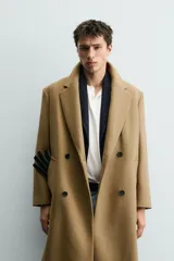 Abrigo largo color camel, de corte relajado (relaxed fit), confeccionado en tejido con mezcla de lana. Presenta cuello con solapas de muesca, manga larga, bolsillos de vivo en cadera, bolsillo interior y cierre frontal de botonadura cruzada.
