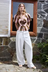 Camisa de rayas verticales rosadas y marrones, con escote en V, mangas corta abullonadas y cierre frontal con múltiples lazadas del mismo tejido. Presenta bajo con acabado de volante.