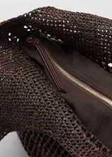 Bolso tipo tote color marrón con diseño de tejido calado de fibra natural, doble asa larga de hombro con detalle de hebilla ajustable y aplique metálico dorado, e incluye un bolso interno de tela con cierre de cremallera.