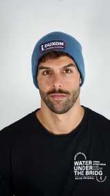 Gorro tipo beanie de punto acanalado en color azul, con parche frontal bordado de la marca Duxon.
