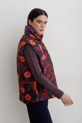 Chaleco puffer con cuello alto y cierre frontal oculto, estampado con diseño floral y de aves en tonos rojos sobre base azul oscuro.