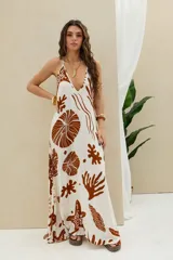 Vestido largo blanco con estampado marrón de temática marina, tirantes finos y escote pronunciado en la espalda.