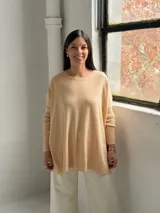 Sweater de punto color beige, de corte holgado y diseño asimétrico con tajos laterales. Presenta cuello redondo y mangas largas con puños acanalados, además de un detalle de costura vertical central.