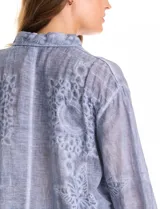 Camisa de algodón color gris con bordados florales en el frente y las mangas. Tiene cuello con solapa y cierre frontal con botones.