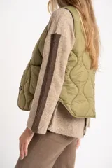 Chaleco capitoneado color verde oliva, con cierre frontal de botones, cuello redondo y diseño acolchado con costuras onduladas.