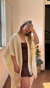 Ruana tejida artesanalmente en telar, color crema o blanco roto, con textura tejida y flecos en los bordes.