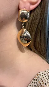 Caravanas colgantes de metal dorado con diseño de dos piezas: una superior redondeada y una inferior con forma de gota irregular.