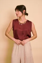 Blusa de satén color bordó, sin mangas, con cuello redondo y detalles de ribete bordado en contraste en las sisas.