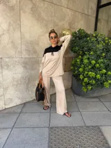 Sudadera con capucha de manga larga, color beige, con canesú negro en la parte superior de los hombros y capucha negra. Presenta cordones negros para ajustar la capucha.