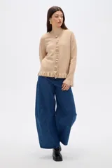 Saco de punto color beige con cuello redondo, cierre frontal con botones y detalle de volados en la tapeta, ruedo y puños.
