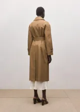 Chaqueta larga de algodón color marrón tostado, estilo gabardina, con cuello camisero, cierre frontal oculto con botones, mangas largas con presillas en los puños y cinturón ajustable con hebilla oscura.