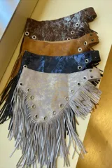 Faja de cuero marrón con detalles plateados, flecos y ojales metálicos.