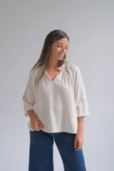 Blusa de corte holgado en color beige, con cuello redondo fruncido y escote en V. Presenta mangas tres cuartos con terminación elástica y un diseño minimalista de textura natural.