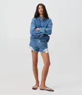 Short de jean tiro medio con encaje floral blanco aplastado en los laterales y dobladillo deshilachado. Cuenta con bolsillos delanteros y traseros, pasacintos y cierre frontal con botón y cremallera.
