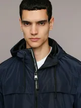 Campera ligera Calvin Klein de corte regular, confeccionada en tejido técnico resistente al viento. Presenta capucha con cordones ajustables, cierre frontal con cremallera, bolsillos laterales con cierre y puños elásticos.