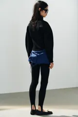 Zapato tipo bailarina deportiva de color negro, con suela de goma y detalle de lazo en la puntera redonda.