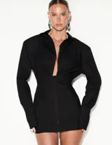 Vestido camisero corto negro, de manga larga con puños anchos, escote en V profundo y detalle de frunces en el busto. Cuenta con cierre frontal de botones y silueta entallada.