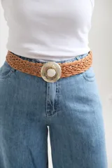 Cinto trenzado de cuero color camel con hebilla metálica circular de estilo artesanal, decorada con un detalle central en piedra clara.