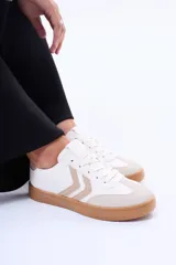 Championes casuales de color blanco con detalles en beige y suela de goma marrón. Presentan diseño clásico con cordones y apliques laterales en zig-zag.