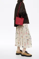 Bolso de mano pequeño tipo tote bag, color rojo, confeccionado en gabardina con detalles en piel. Posee asas de mano y correa ajustable para llevar al hombro o cruzado. Lleva placa metálica con el logo de la marca en el frente.