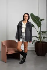 Campera de jean color negro lavado, de corte oversize, con detalle de tachas metálicas plateadas dispuestas en líneas verticales a lo largo de la prenda, cuello clásico, cierre frontal con botones metálicos y bolsillos en el pecho.