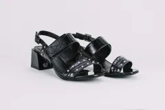 Sandalias negras de cuero charol con dos tiras, una sobre los dedos y otra sobre el empeine, ambas con apliques de tachas plateadas. Tira trasera con hebilla. Taco cuadrado.