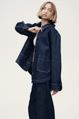 Campera camisera en denim rígido color azul, con cuello camisero, cierre frontal de botones, bolsillos de parche delanteros y bajo redondeado.
