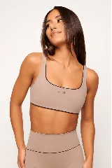 Top deportivo color beige con contorno negro, breteles anchos y logo pequeño en el frente.