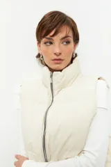 Chaleco puffer color beige, sin mangas, con cuello alto y cierre frontal con cremallera.