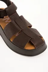Sandalias estilo cangrejera de cuero marrón con plataforma, tiras cruzadas en el empeine, tira ajustable con hebilla metálica en el tobillo y detalle de estrella dorada grabada.